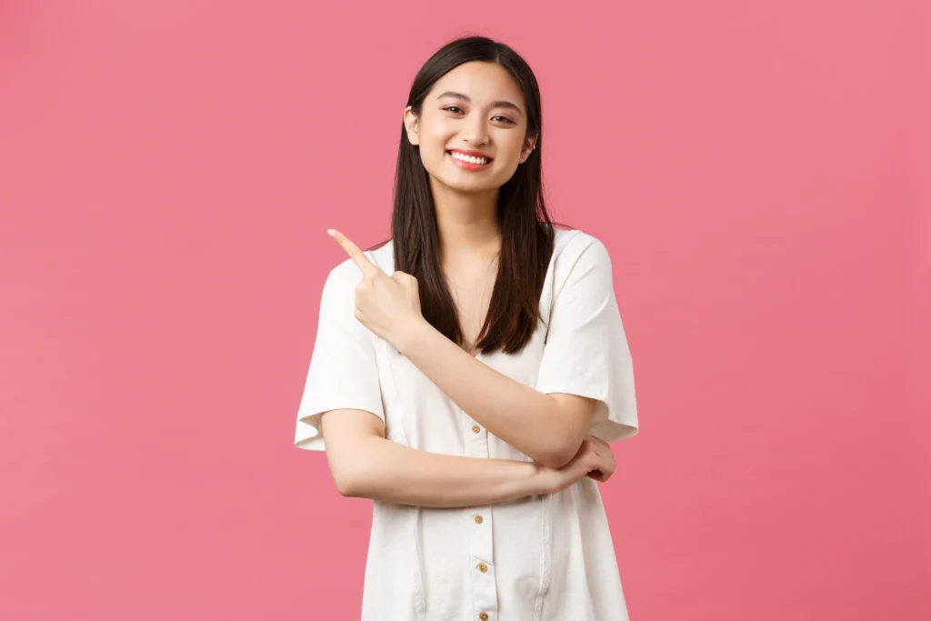 Skincare Brand Landing Page Concept beauty people emotions summer leisure vacation concept tender beautiful asian girl white dress pointing finger upper left corner inviting take look new promo offer pink background.webp