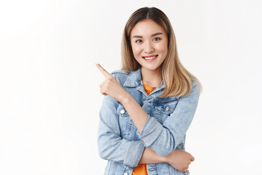 Skincare Brand Landing Page Concept confident stylish good looking asian blond girl recommend follow her direction pointing upper left corner index finger smiling camera self assured white wall.webp